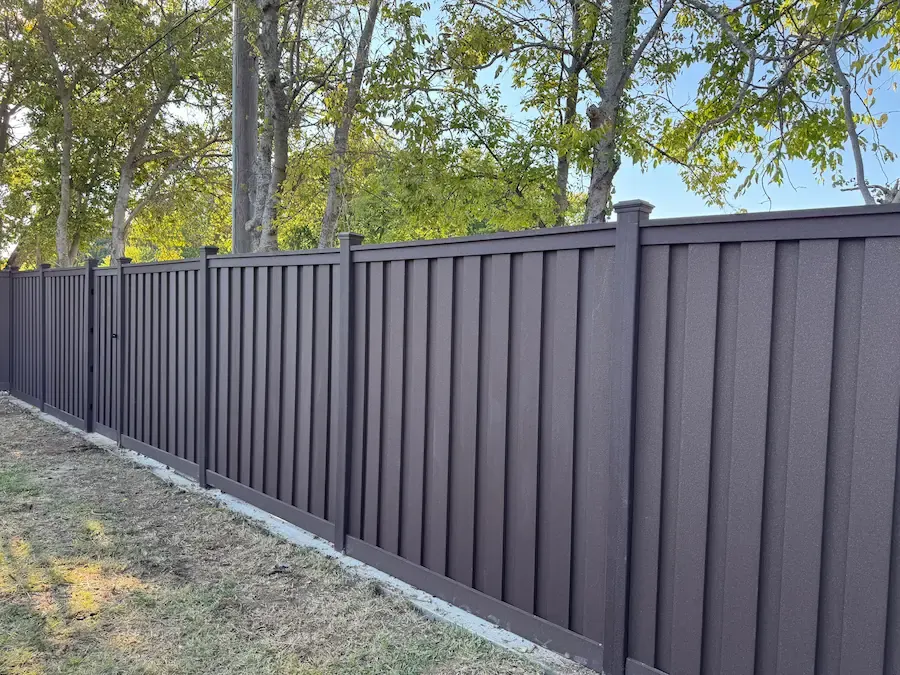 Dark gray vertical privacy fence along a tree line
